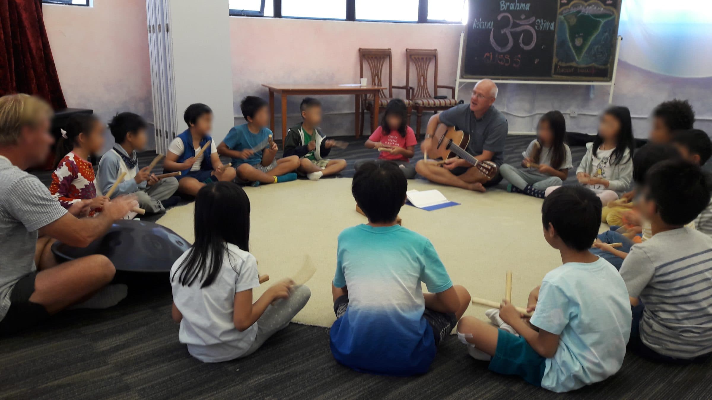 Children sitting in a circle with rhythm sticks while Markus Weiss plays guitar